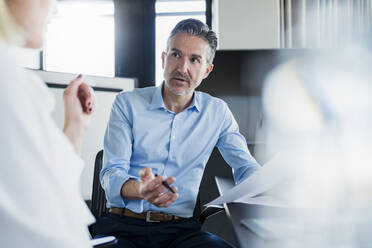 Male entrepreneur gesturing while discussing with female coworker sitting in office - DIGF15617