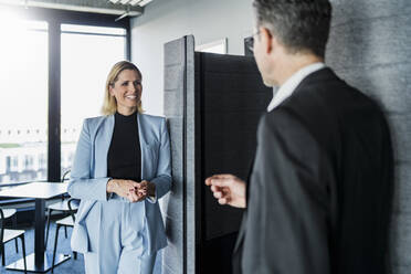 Lächelnde Geschäftsfrau, die einen männlichen Kollegen anschaut, während sie im Büro diskutiert - DIGF15626