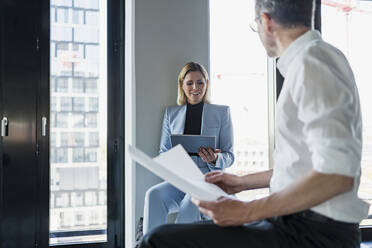 Smiling businesswoman using digital tablet while discussing with male colleague in office - DIGF15638