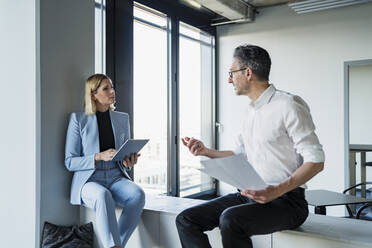 Mature businessman discussing with female colleague while sitting on furniture in office - DIGF15640