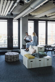 Geschäftsmann und Geschäftsfrau, die zusammen diskutieren, während sie auf Möbeln im Büro sitzen - DIGF15642