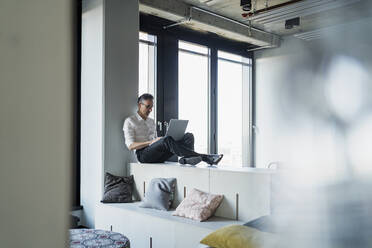 Mature businessman using laptop while sitting on furniture in office - DIGF15643