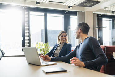 Lächelnde Geschäftsfrau mit Blick auf einen männlichen Kollegen, der in einem kreativen Büro diskutiert - DIGF15649