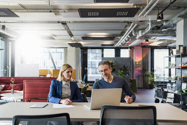 Männliche und weibliche Mitarbeiter diskutieren über einen Laptop, während sie am Schreibtisch in einem kreativen Büro sitzen - DIGF15651