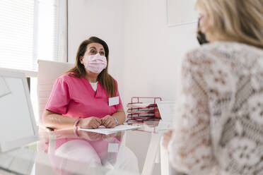 Kosmetikerin mit Gesichtsschutzmaske im Gespräch mit einer Frau in einer Klinik - EGAF02384
