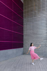Young woman dancing in front of shutter on footpath - TCEF01889