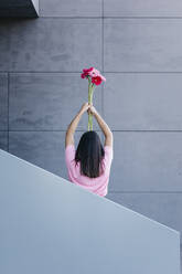 Junge Frau hält einen Blumenstrauß vor einer grauen Wand - TCEF01897