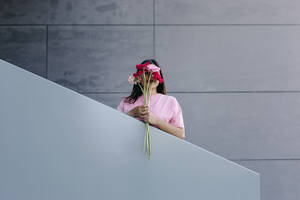 Frau hält einen Strauß Gerbera-Gänseblümchen vor dem Gesicht am Geländer - TCEF01899