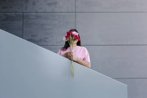 Woman holding bunch of Gerbera daisies in front of face at railing - TCEF01899