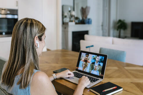 Freiberufliche Mitarbeiterin mit drahtlosen Kopfhörern, die zu Hause über einen Laptop eine Videokonferenz abhält - XLGF01944