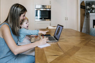 Junge, der mit seiner Mutter während einer Online-Arztkonsultation über einen Laptop zu Hause sitzt und auf etwas zeigt - XLGF01949