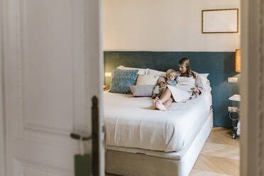 Pregnant woman showing photo album to son while sitting in bedroom at home - XLGF01955