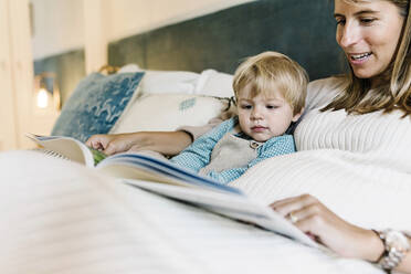 Lächelnde erwachsene Frau zeigt ihrem Sohn ein Fotoalbum, während sie zu Hause auf dem Bett sitzt - XLGF01956