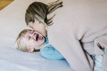 Woman kissing playful son on bed at home - XLGF01959