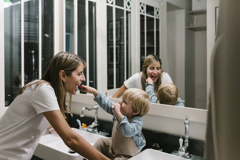 Boy brushing mother's teeth in bathroom at home - XLGF01961