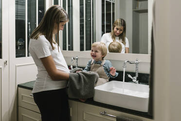 Schwangere Frau trocknet die Hände ihres Sohnes mit einem Handtuch im Badezimmer zu Hause - XLGF01962