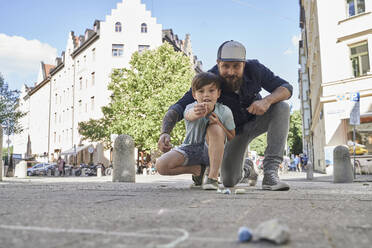 Vater und Sohn spielen mit Steinen auf dem Bürgersteig in der Stadt - AUF00679