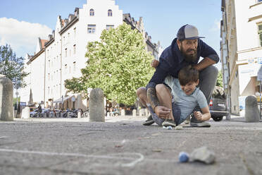 Vater und Sohn spielen mit Kreide auf dem Bürgersteig in der Stadt - AUF00680