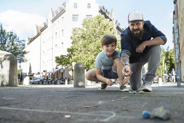 Vater wirft mit Kreide, während er mit seinem Sohn auf dem Gehweg spielt - AUF00681