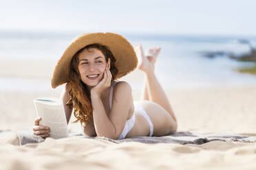 Lächelnde schöne Frau mit Buch Tag träumen, während auf Sand während sonnigen Tag liegen - SBOF03853