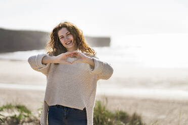 Smiling young woman showing heart shape at beach - SBOF03864