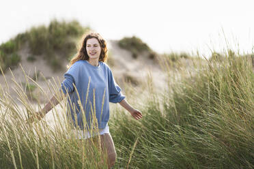Young woman with arms outstretched walking in dunes - SBOF03879