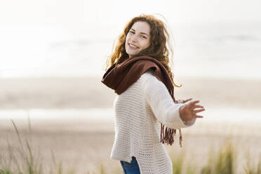 Happy woman with arms outstretched standing at beach - SBOF03884