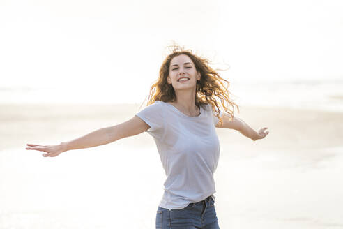 Carefree woman with arms outstretched spinning around at beach - SBOF03892