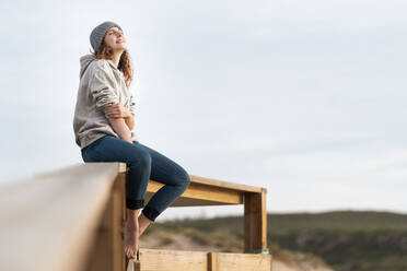 Woman with eyes closed sitting on railing during vacations - SBOF03897
