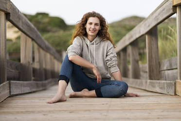 Young woman sitting on wooden bridge during vacations - SBOF03900