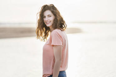 Beautiful woman looking over shoulder while standing at beach during sunny day - SBOF03903