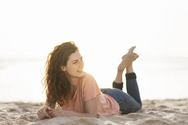 Young woman looking away while lying on sand during sunny day - SBOF03906