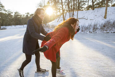 Young man assisting girlfriend with ice-skating on frozen lake - FVDF00198