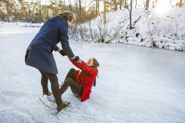 Boyfriend holding hands of girlfriend while getting up on frozen lake - FVDF00199