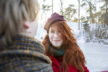 Smiling redhead woman wearing knit hat looking at boyfriend - FVDF00203
