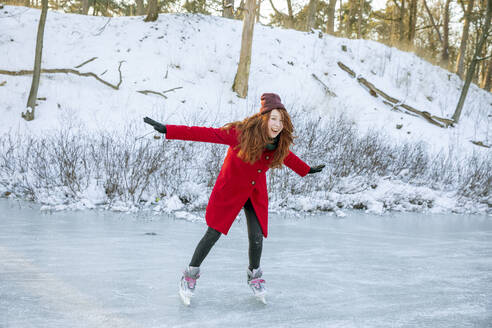 Fröhliche Frau mit ausgestreckten Armen genießt das Schlittschuhlaufen auf einem zugefrorenen See - FVDF00206