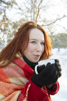 Rothaarige Frau hält Kaffee in der Hand und schaut im Winter weg - FVDF00215