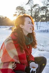 Junge Frau hält Kaffeetasse und schaut im Winter weg - FVDF00218
