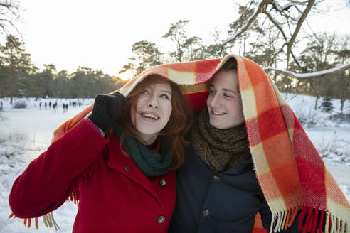 Lächelndes Paar, das im Winter den Kopf mit einer Decke bedeckt - FVDF00220