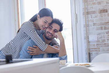 Smiling girlfriend embracing boyfriend in domestic kitchen - EIF01074