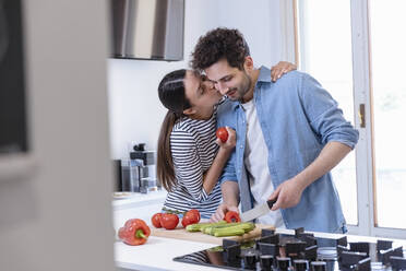 Junge Frau küsst ihren Freund auf die Wange, während sie in der heimischen Küche Paprika schneidet - EIF01084