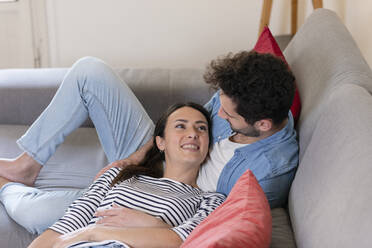 Lächelnde Freundin schaut ihren Freund an, während sie zu Hause auf dem Sofa liegt - EIF01096