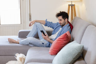 Mid adult man using mobile phone while sitting on sofa at home - EIF01097