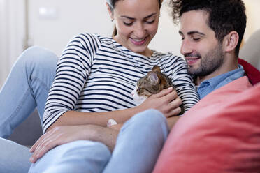 Smiling couple with tabby cat in living room at home - EIF01100