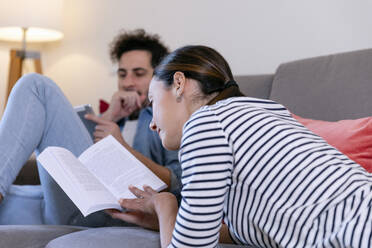 Eine Frau liest ein Buch und ein Mann benutzt ein digitales Tablet auf dem Sofa zu Hause - EIF01103