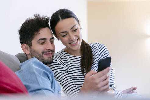 Lächelndes Paar, das ein Mobiltelefon im heimischen Wohnzimmer benutzt - EIF01108