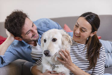 Lächelndes Paar streichelt Hund im Wohnzimmer zu Hause - EIF01113