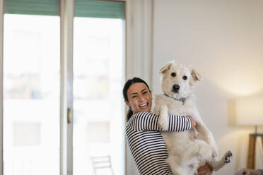 Cheerful female owner holding dog at home - EIF01123