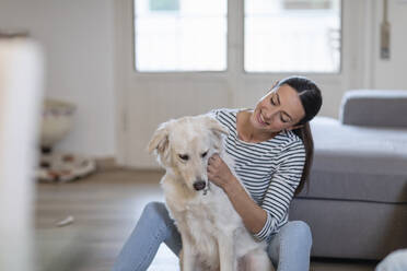 Young woman stroking cute dog in living room - EIF01125