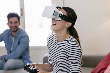 Young woman laughing while playing with virtual reality simulator at home - EIF01129